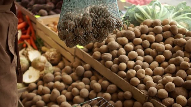 Woman puts their hands in a string bag new potatoes from wooden boxes on the market. Eco packaging, zero waste