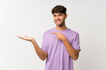 Young handsome man over isolated white background holding copyspace imaginary on the palm to insert...
