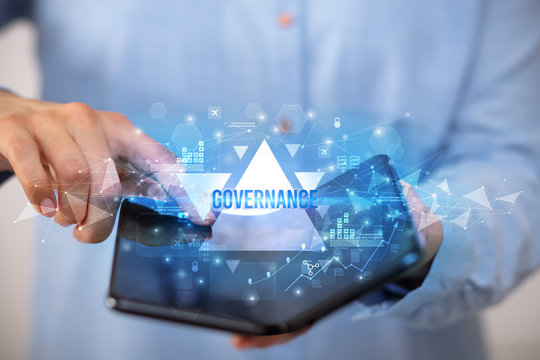Businessman holding a foldable smartphone with GOVERNANCE inscription, business concept - Powered by Adobe