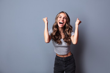 Rejoicing young woman screaming with joy celebrating victory win success isolated on grey background.