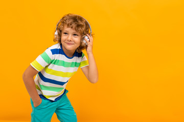 cheerful curly schoolboy on an orange background in headphones