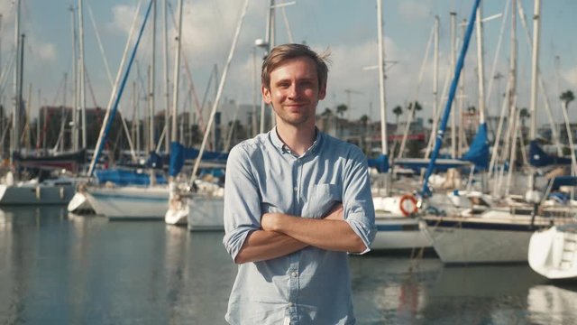Man dressed in casual wear near yacht. Happy adult bearded yachtsman close-up portrait. Handsome sailor smiling during regata on a sea or river.