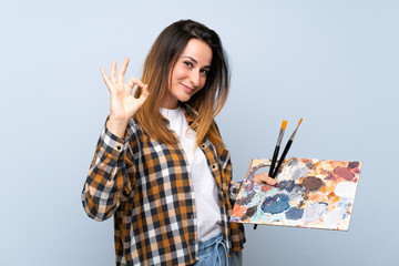 Young painter woman over isolated blue background showing ok sign with fingers