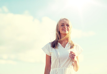 country, nature, summer holidays, vacation and people concept - smiling young woman in white dress over blue sky