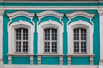 Fragment of the facade of an old mansion - a green wall with three white windows framed by stucco