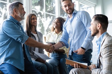 Welcome to our team! Business men in smart casual wear shaking hands while working in the creative office.