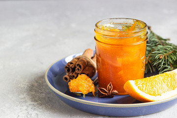 Homemade orange jam with orange peel in a glass jar as a gift for Christmas or New year with fir branches, spices (cinnamon and anise) and orange. Selective focus.