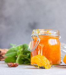 Orange jam or marmalade in glass jar, fresh and dried orange fruit slices, mint and spices on light grey background.