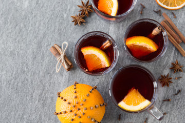 christmas and seasonal drinks concept - hot mulled wine, dry orange slices, raisins with cashew nuts and aromatic spices on grey background