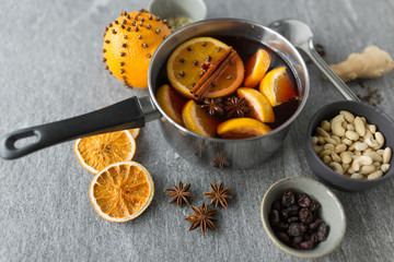 christmas and seasonal drinks concept - pot with hot mulled wine, orange slices, aromatic spices, nuts and ladle on grey background