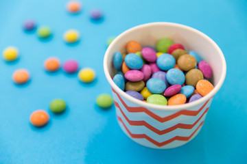 food, confectionery and sweets concept - candy drops in paper cup on blue background