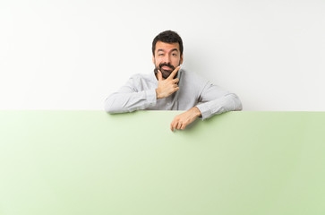 Young handsome man with beard holding a big green empty placard thinking