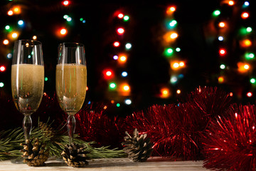 Romantic Christmas and New Year dinner of a couple in love with two glasses of champagne. Red tinsel and spruce branch with a cone on a table on a dark background with blurred lights. Copy space.