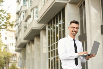 Fototapeta premium Portrait of handsome businessman with laptop outdoors
