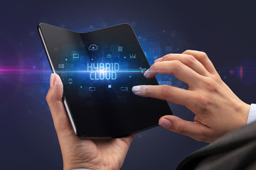 Businessman holding a foldable smartphone with HYBRID CLOUD inscription, cyber security concept