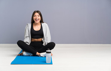 Fototapeta premium Young sport woman sitting on the floor with mat with surprise facial expression