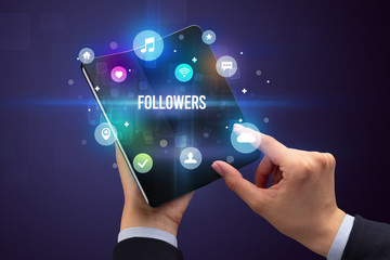 Businessman holding a foldable smartphone with FOLLOWERS inscription, social media concept