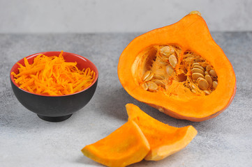 Half a raw pumpkin, sliced pumpkin and grated pumpkin. Light background. Close-up.