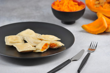 Pumpkin stuffed ravioli. One of the ravioli is broken to show the filling. In the background are half a pumpkin and a grated pumpkin. Close-up.