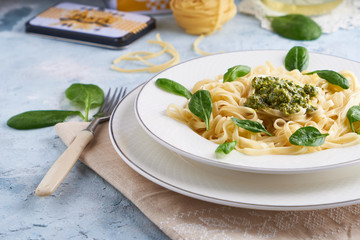 Appetizing pasta with sauce pesto and spinach in plate on light blue stone table.