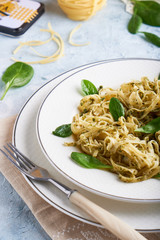 Appetizing pasta with sauce pesto and spinach in plate on light blue stone table