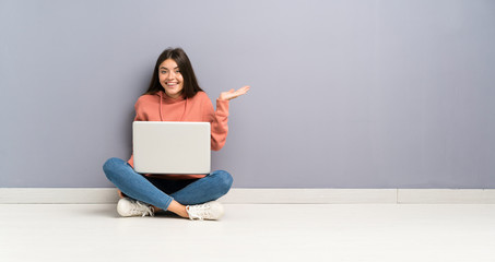 Young student girl with a laptop on the floor holding copyspace imaginary on the palm