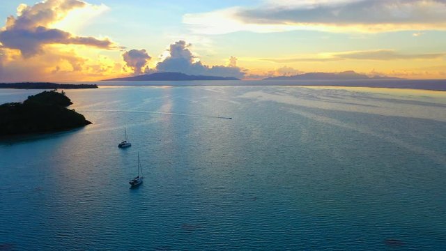 Aerial of an awesome sunset over the ocean, drone flying forward then turning from left to right and tilting down while descending to follow a boat - Bora Bora, French Polynesia