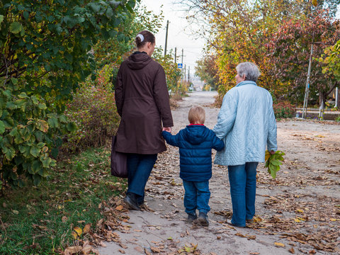 Family on walk. Grandmother, mother and child walk along alley in village. Autumn and fallen leaves