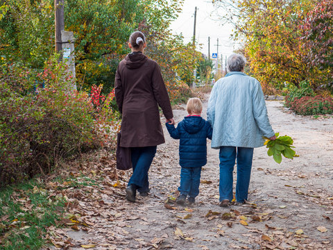 Family on walk. Grandmother, mother and child walk along alley in village. Autumn and fallen leaves