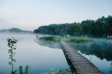 Fog, grass, trees against the backdrop of lakes and nature. Fishing background. Misty morning. nature. Wild areas. bridge over the river the island. tent, umbrella. swamp.