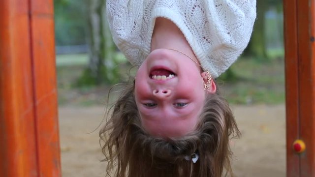 Girl hanging upside down on the horizontal bar.