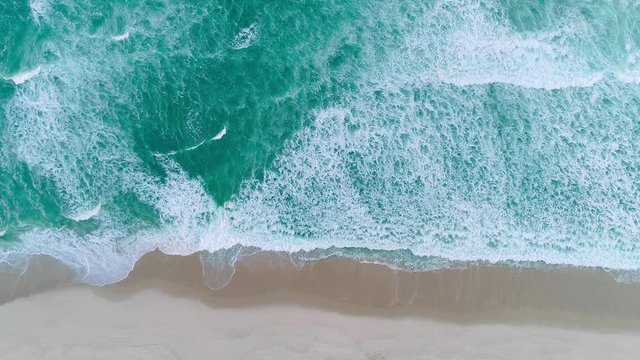 Aerial locked shot of waves breaking on the shore. Colourful beach umbrellas and people enjoying the summer. 4K.