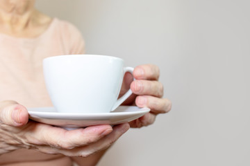 A senior woman holding a cup of coffee or tea in hands, copy space