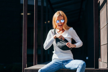 Stylish model girl at the city in black leather jacket and white sweater and glasses with waist bag