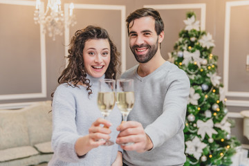 Toasting with champagne glasses against holiday lights and christmas tree.