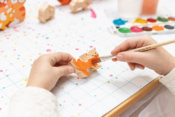 Children's hands paint a wooden toy with a watercolor brush