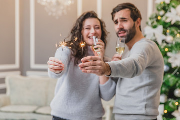 Concept of parties and entertainment. Sweet photo of energetic couple celebrating, with champange in lovely new year decorated room.