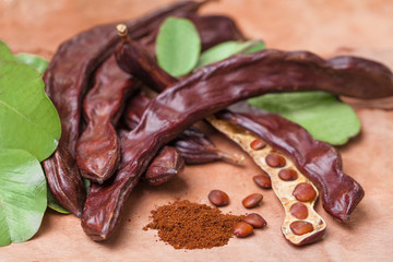 Carob. Organic carob pods with seeds and leaves on tree bark table. Healthy eating, food background.