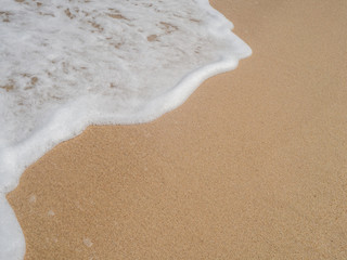 Wave with white foam rolls onto the sand of a beach