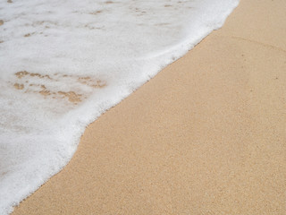 Wave with white foam rolls onto the sand of a beach