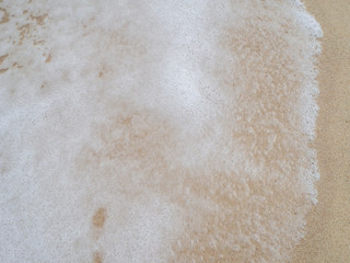 Wave with white foam rolls onto the sand of a beach