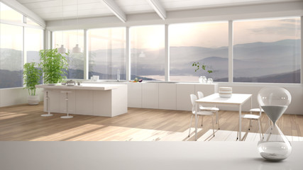 White table or shelf with crystal hourglass measuring the passing time over minimalist kitchen with island and stools and window, architecture interior design, copy space background