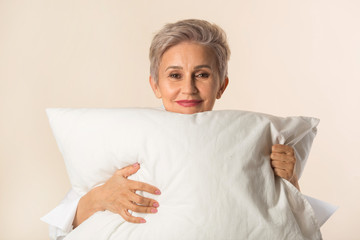 stylish beautiful aged woman with a pillow in hands on a beige background
