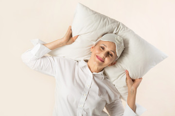 stylish beautiful aged woman lies on a pillow in a white shirt on a beige background