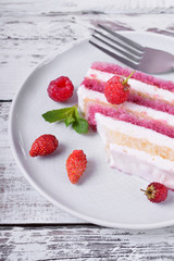 Piece of cake with many layers topped with fresh berries on a ceramic plate