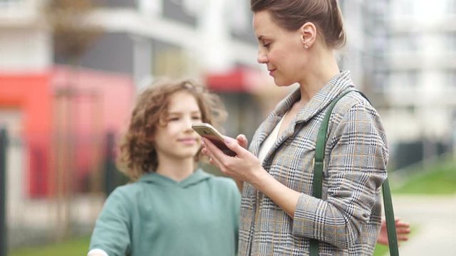 Mature business woman on a city street looking at a smartphone. Her teenage curly son comes up and they hugging joyfully. Mothers Day