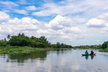 Asian couple paddle wooden row boat for across the river in countryside with woods and blue sky background. feel relax and clam folkways concept, landscape background.
