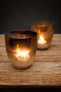 2 smoked glass tea light holders and glowing candles, shot on a wooden table