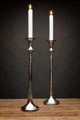 2 tall silver candle holders and glowing candles, shot on a wooden table