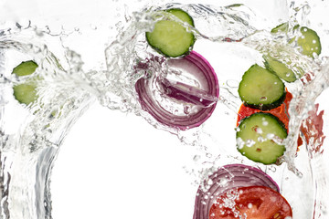 Cucumber slices and tomato, onion, fallen in water on a white background, top view
